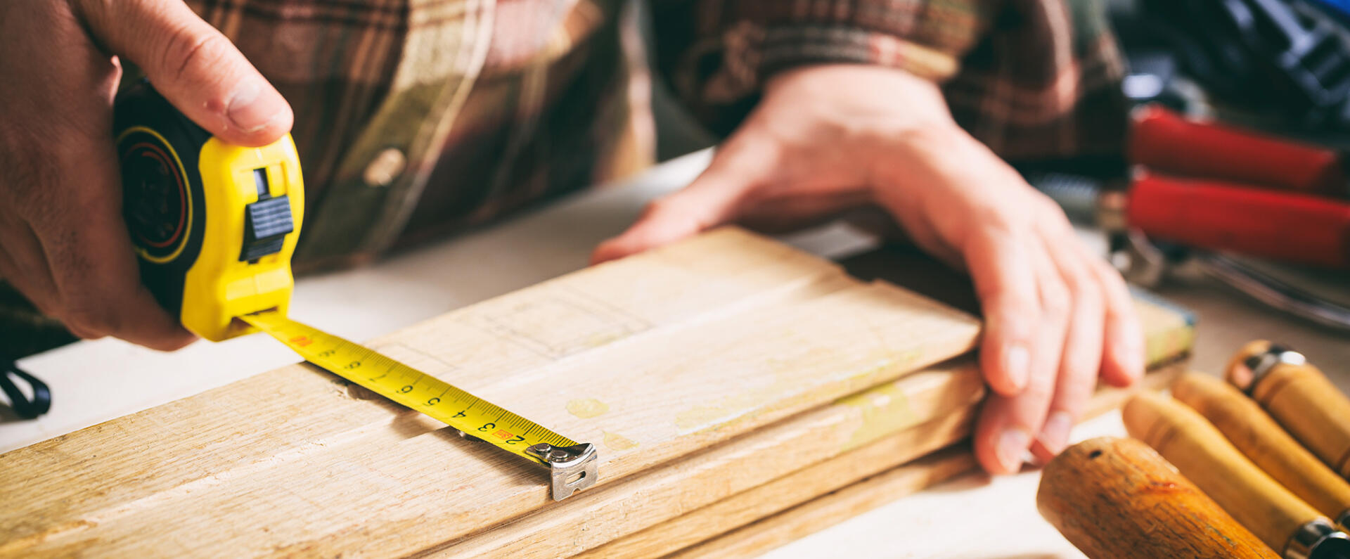Man measuring a plank of wood with a tape measure
